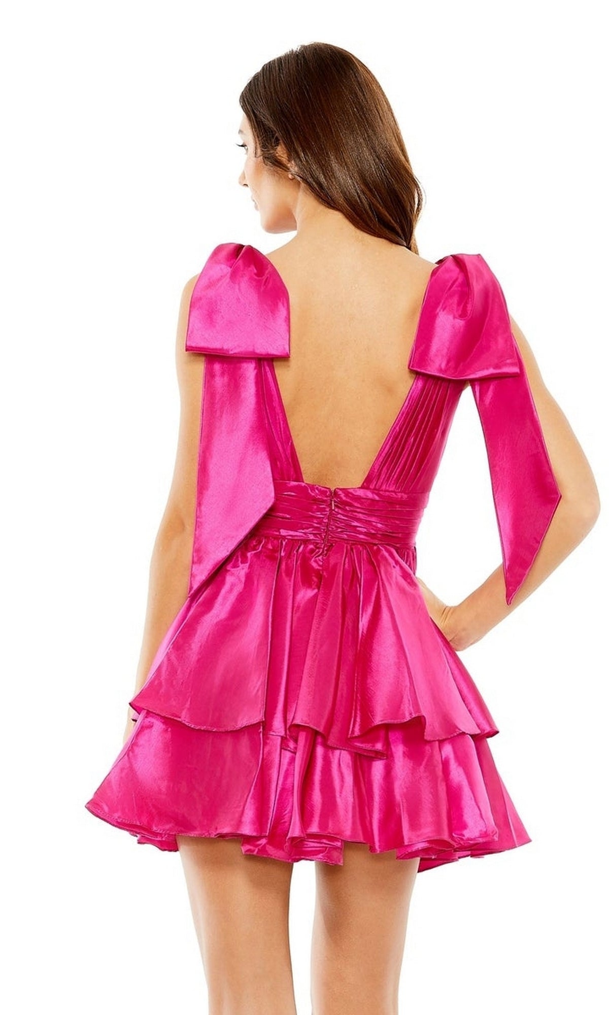 A woman photographed from behind wears the Mac Duggal 11657 Bow Short Ruffled Hoco Dress in bright pink, featuring an open back, tiered ruffles, and large bow shoulder details.